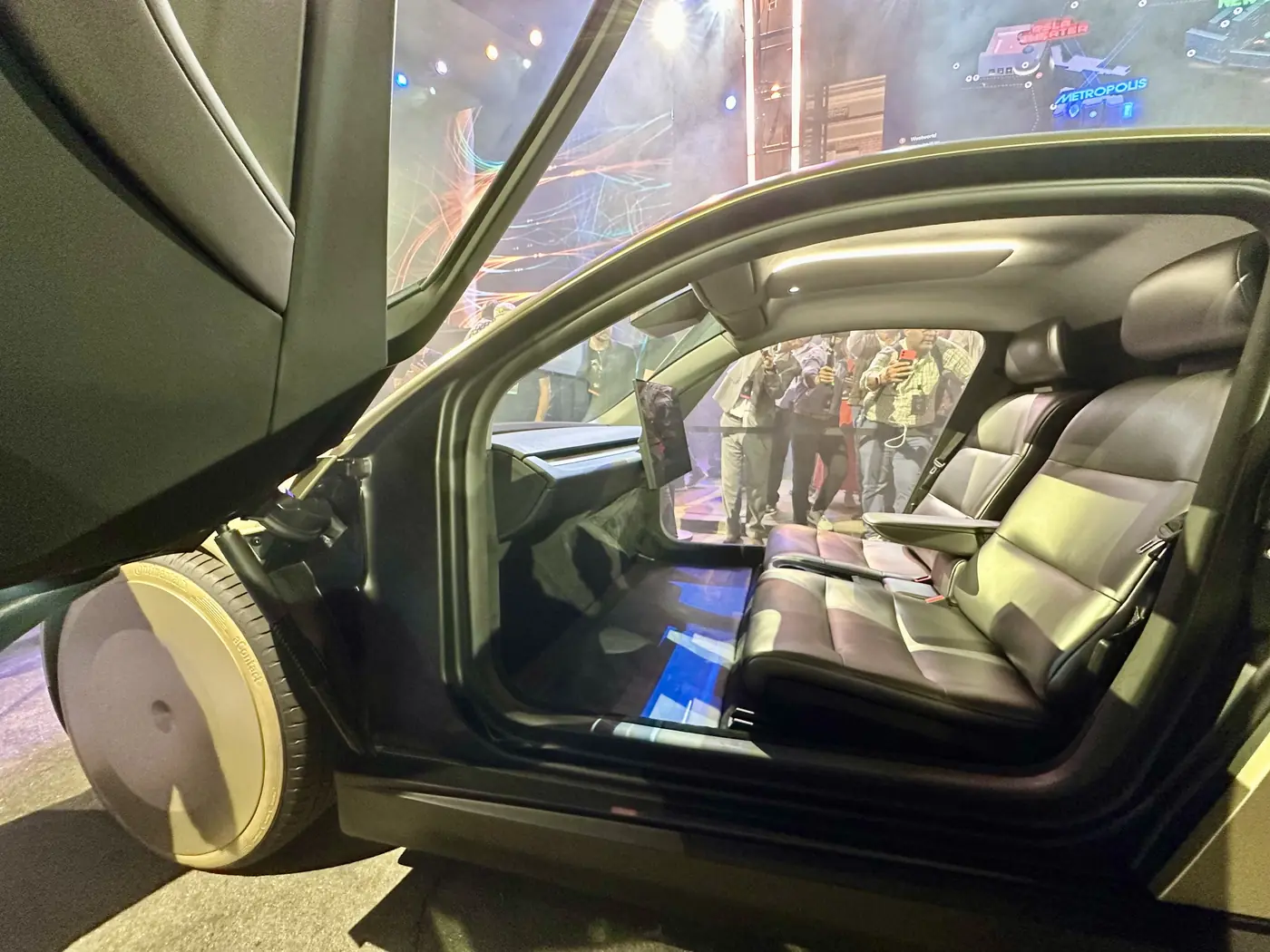 Cabin of a Cybercab, with two light-colored seats, no steering wheel, and a wide screen across the front.