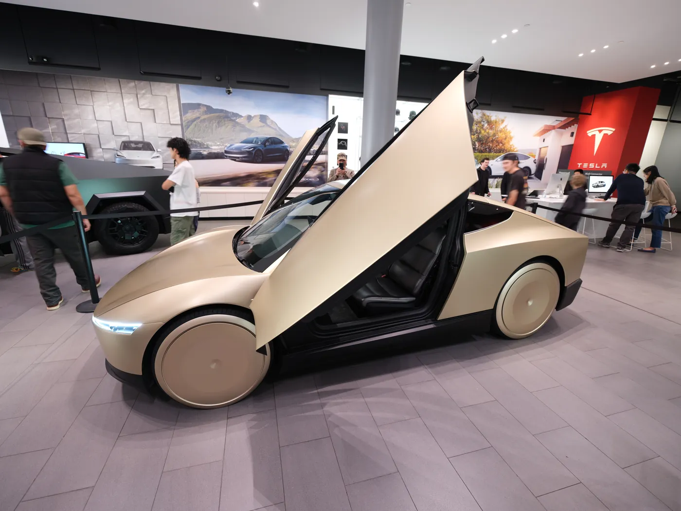 Three-quarter view of a silver Cybercab parked outdoors, with a broad glass canopy and a smooth body.